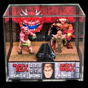 May include: A 3D shadow box diorama featuring a pixelated video game scene with a first-person perspective of a weapon, various monster figures, and a status bar displaying 72% HEALTH, ARMS, and 68% ARMOR with a central character portrait.