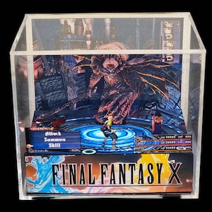 May include: A Final Fantasy X diorama in a clear acrylic display case. The scene depicts a battle with characters and a monster. The game's title is displayed at the bottom. The diorama is a collectible item.
