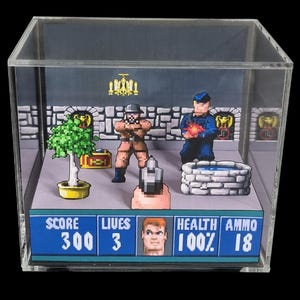 May include: A 3D diorama of a pixelated video game scene encased in a clear acrylic cube. The display features a stone wall background, a potted green plant, a stone well, and two pixelated characters. A game interface shows SCORE 300, LIVES 3, HEALTH 100%, and AMMO 18.