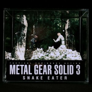 Puede incluir: Un diorama que representa una escena del videojuego Metal Gear Solid 3: Snake Eater. El diorama presenta dos figuras, una con un traje de camuflaje y la otra con un traje blanco, de pie en un bosque nevado. El diorama est&aacute; encerrado en una caja de pl&aacute;stico transparente con una base negra que dice "Tactical Espionage Action Metal Gear Solid 3 Snake Eater".