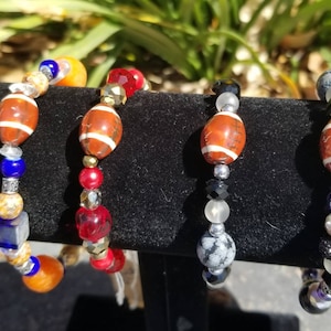 May include: Four beaded bracelets with football-shaped charms. The bracelets are made with various colors of beads, including blue, red, orange, black, and white.