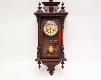 Reloj de pared antiguo con movimiento y péndulo en caja de madera.