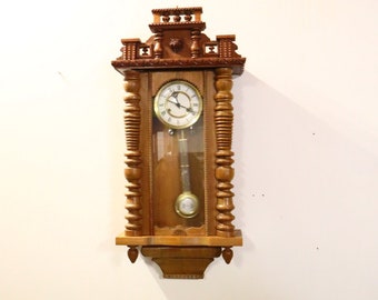 Reloj de pared antiguo con movimiento y péndulo en caja de madera.