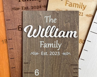 May include: Three wooden growth charts with personalized family names and establishment dates. The charts feature the names "Daniel Family Est. 2024", "The William Family Est. 2023", and "Abraham Family 21".