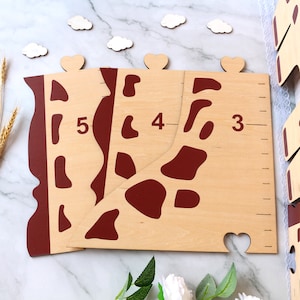 May include: Wooden giraffe growth chart with red spots and numbers 3, 4, and 5. The chart is made of light wood and has a brown stain.