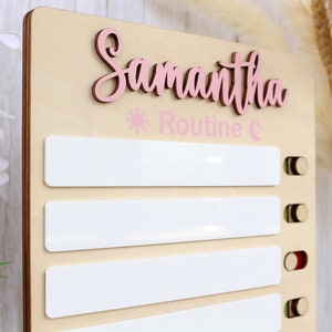 May include: A light wood personalised daily routine chart with the name Samantha in pink lettering. The chart has five white spaces for writing in a daily routine and a sun and moon icon with the word "Routine" in pink lettering.