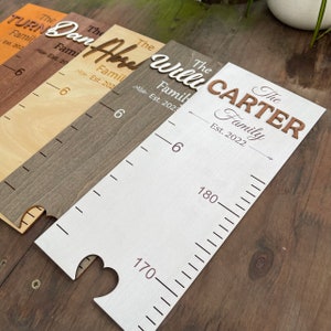 May include: Four white wooden growth charts with different family names and establishment dates. The names are "The Turner Family Est. 202", "The Dan Family Est. 20", "The And Family Est. 202", and "The Will Carter Family Est. 2022". Each chart has a heart-shaped cutout at the bottom and a ruler with markings in centimetres.