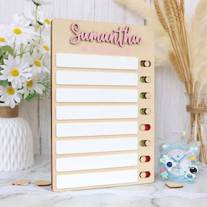 May include: A wooden board with a white background and a pink inscription that reads "Samantha's Routine". The board has eight white spaces for writing with red, green, and yellow circles next to each space.