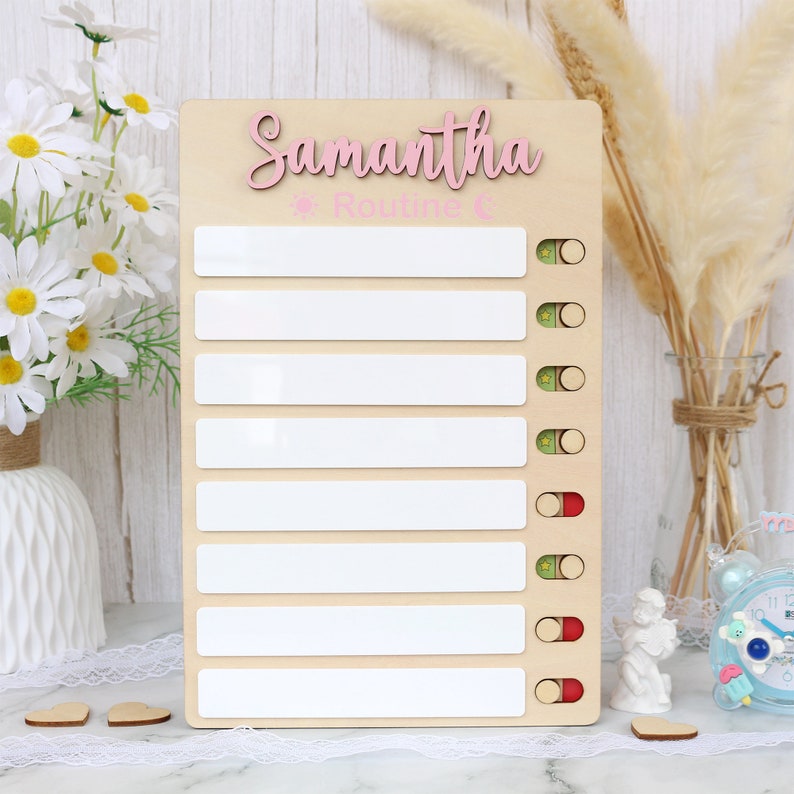 May include: A wooden checklist with the name Samantha written in pink letters. The checklist has eight blank lines with a sun and the word "Routine" written above the lines. Each line has a green and red circle next to it.