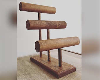 May include: A wooden jewelry stand with three tiers of round rods for displaying bracelets. The stand is made of dark brown wood and has a rectangular base.