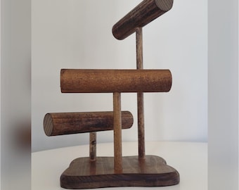 May include: Wooden jewelry stand with three horizontal bars for displaying bracelets and bangles. The stand has a dark brown finish and a unique, irregular base.