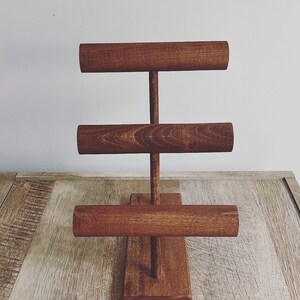 May include: A wooden jewelry stand with three tiers of round rods for displaying bracelets and bangles. The stand is stained a dark brown color.