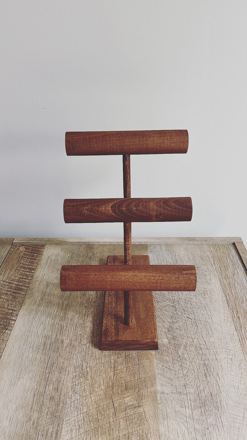 May include: A wooden jewelry stand with three tiers of round rods for displaying bracelets and bangles. The stand is stained a dark brown color.