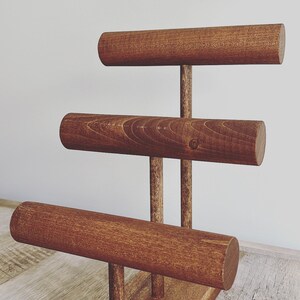 May include: A wooden jewelry stand with three tiers for displaying bracelets. The stand is made of dark brown wood and has a rectangular base.