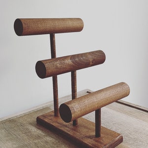 May include: A wooden jewelry stand with three tiers for displaying bracelets. The stand is made of dark brown wood and has a simple, modern design.