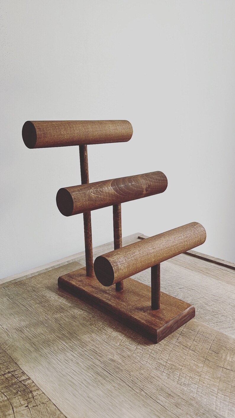 May include: A wooden jewelry stand with three tiers for displaying bracelets. The stand is made of dark brown wood and has a simple, modern design.