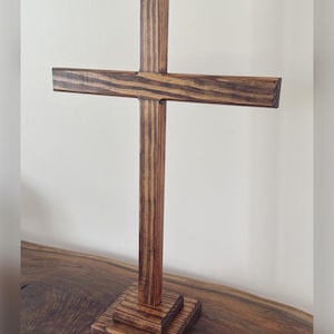 May include: A wooden cross with a dark brown stain. The cross is standing on a wooden base.