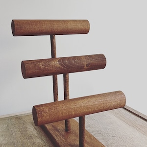 May include: A wooden jewelry stand with three tiers for displaying bracelets. The stand is made of dark brown wood and has a rectangular base.