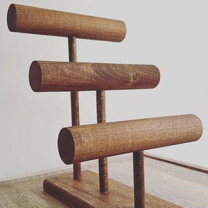May include: A wooden jewelry stand with three tiers of rounded rods for displaying bracelets or bangles. The stand has a rectangular base and is made of dark brown wood.
