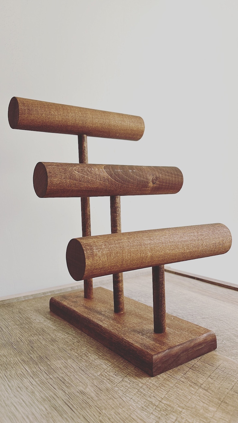 May include: A wooden jewelry stand with three tiers of rounded rods for displaying bracelets or bangles. The stand has a rectangular base and is made of dark brown wood.