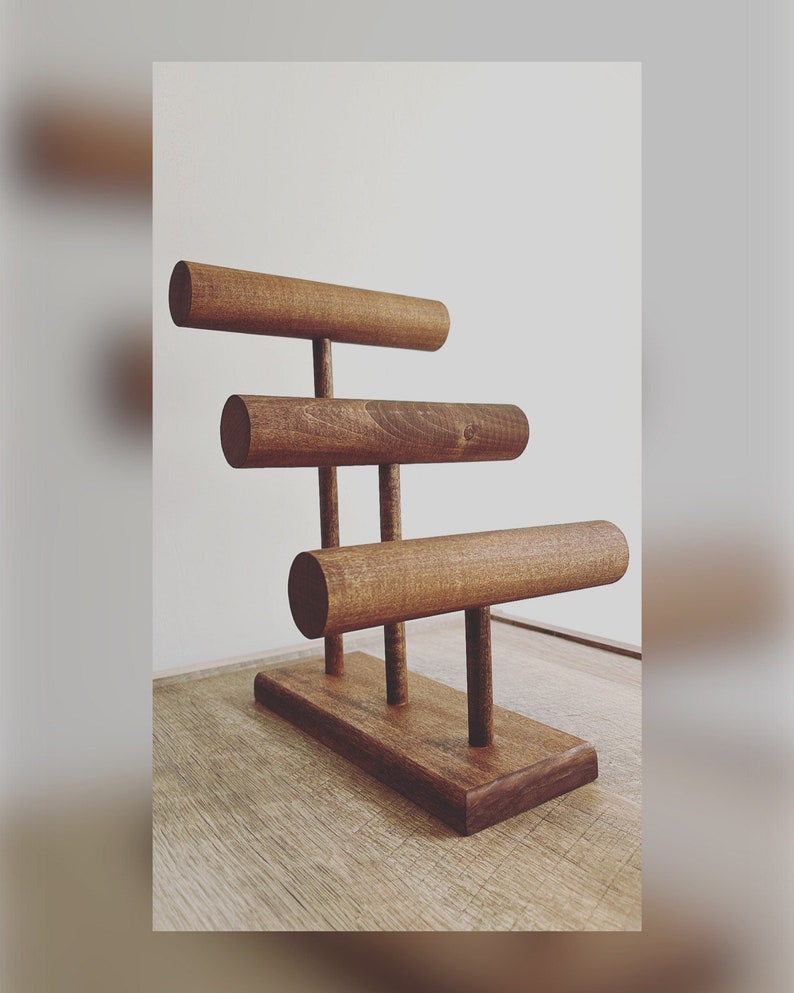 May include: A wooden jewelry stand with three tiers of round rods for displaying bracelets. The stand is made of dark brown wood and has a rectangular base.
