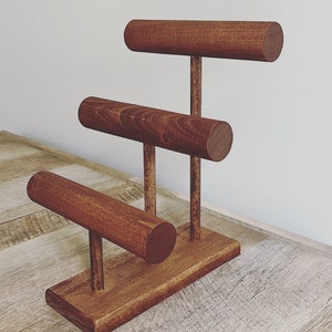 May include: A wooden jewelry stand with three tiers for displaying bracelets. The stand is made of dark brown wood and has a simple, modern design.