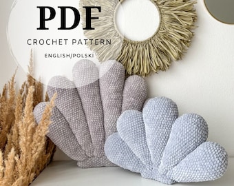 May include: A PDF crochet pattern document featuring two shell-shaped pillows. One pillow is a light gray, and the other is a slightly darker gray. Both pillows have a textured, plush surface and are shaped like a fan with multiple rounded segments.