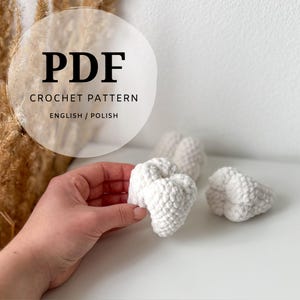 Könnte beinhalten: Nahaufnahme von drei weißen gehäkelten Herzen, eines davon wird in einer Hand gehalten. Das Bild enthält den Text "PDF CROCHET PATTERN ENGLISH / POLISH". Die Herzen befinden sich auf einer weißen Oberfläche.