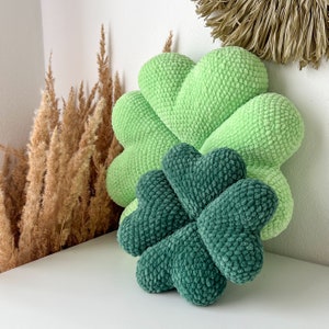 May include: Two crocheted pillows shaped like four-leaf clovers. The larger pillow is light green and the smaller pillow is dark green.