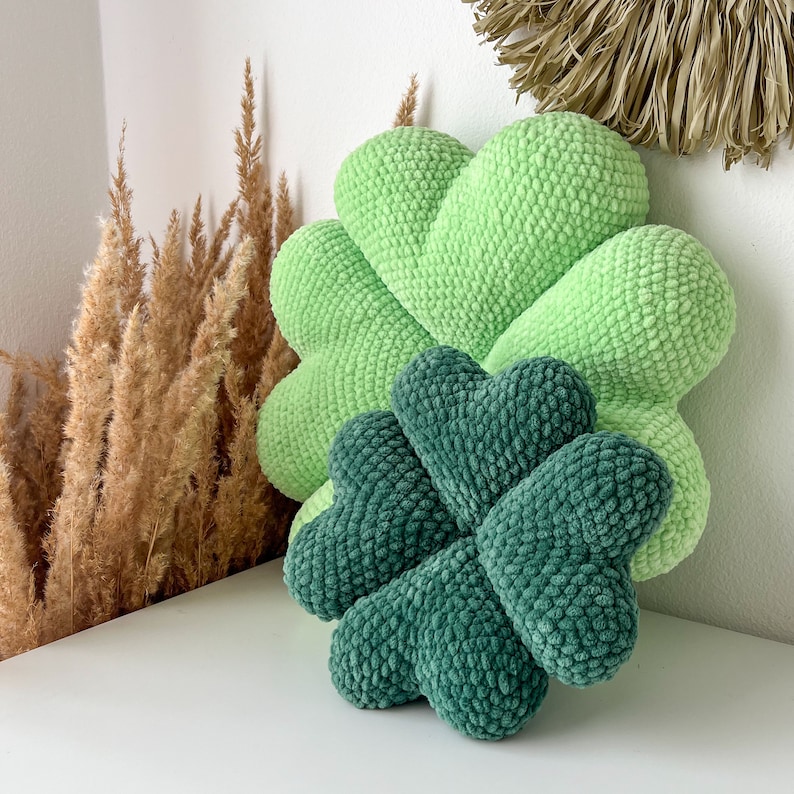 May include: Two crocheted pillows shaped like four-leaf clovers. The larger pillow is light green and the smaller pillow is dark green.