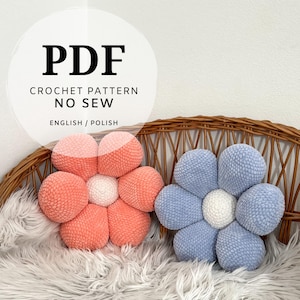 May include: Two plush, flower-shaped crochet cushions in coral and blue, with white centres, rest on a fluffy white surface. The cushions are displayed on a wicker chair. The image includes the text "PDF CROCHET PATTERN NO SEW ENGLISH / POLISH."