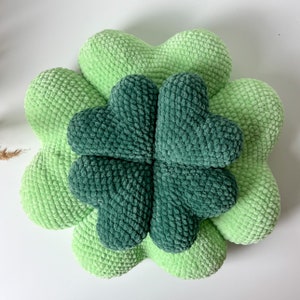 May include: A green crocheted four-leaf clover pillow. The pillow is made of soft, fluffy yarn and is perfect for adding a touch of whimsy to any room.