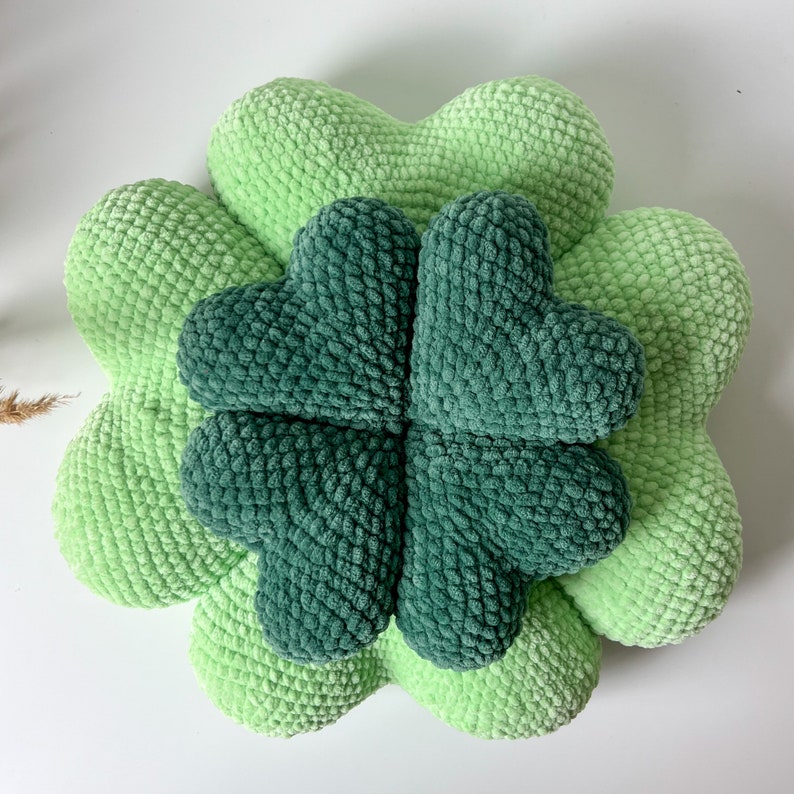 May include: A green crocheted four-leaf clover pillow. The pillow is made of soft, fluffy yarn and is perfect for adding a touch of whimsy to any room.