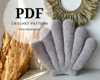 May include: A light gray, plush, shell-shaped pillow with a textured, velvety surface. The image includes text that reads PDF CROCHET PATTERN ENGLISH/POLSKI, indicating a digital document for creating this specific seashell-shaped cushion design.