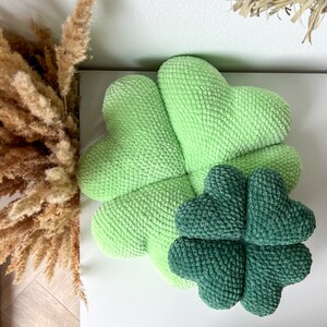 May include: A green crocheted four-leaf clover pillow with a smaller green crocheted four-leaf clover pillow inside.