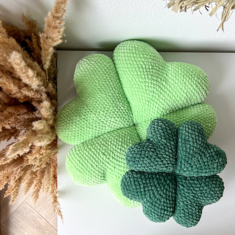 May include: A green crocheted four-leaf clover pillow with a smaller green crocheted four-leaf clover pillow inside.