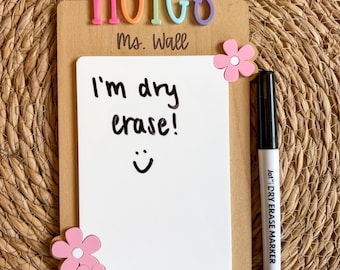 May include: A rectangular wooden dry erase board featuring the word NOTES in colorful 3D letters at the top, the text Ms. Wall, and three pink flower accents. The white board surface displays the handwritten text I'm dry erase! with a smiley face.