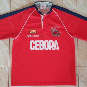 May include: Red rugby shirt with navy blue sleeves and white trim. The shirt displays the word "CEBORA" in white, along with logos and text including "TETLY'S BITTER" and "WILLOWS CENTENARY".
