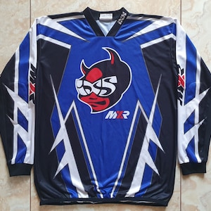 Puede incluir: Una camiseta de manga larga azul, negra y blanca con un diseño de diablo y los textos "ISS" y "MXR". La camiseta tiene cuello en V y está hecha de un material brillante y deportivo. Ideal para deportes.