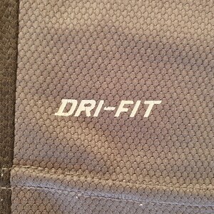 Puede incluir: Primer plano de una camiseta deportiva gris con el texto "DRI-FIT" en blanco. La camiseta tiene un patr&oacute;n texturizado en forma de panal. Un panel gris m&aacute;s oscuro es visible en el lado izquierdo de la imagen.