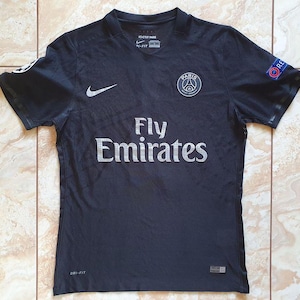 Pode incluir: Camisola de futebol preta de manga curta com a inscrição "Fly Emirates" em prata. A camisola apresenta o logótipo do Paris Saint-Germain e um logótipo da Nike. A manga tem um patch "RESPECT".