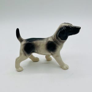 Puede incluir: Figura de cerámica de un perro en posición de pie. El perro tiene la cabeza y las orejas negras, con manchas negras en la espalda y los lados. Las patas y el vientre son blancos. La cola del perro está levantada.