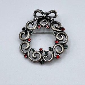 May include: Silver tone Christmas wreath brooch with red and green rhinestones and a bow.