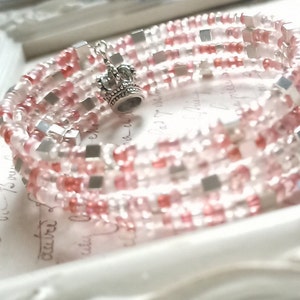 May include: A multi-strand bracelet made of pink and clear beads with silver accents. The bracelet has a crown charm.