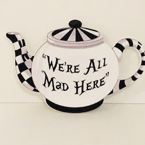 May include: White teapot with a black and white chequered pattern. The teapot has a quote on the front that reads "We're All Mad Here".