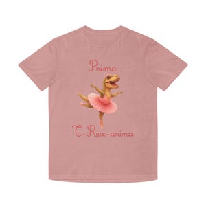 May include: A dusty rose short-sleeved t-shirt featuring a graphic of a Tyrannosaurus Rex wearing a pink tutu and ballet slippers. The text "Prima" is printed above the dinosaur, and "C-Rex-arina" is printed below in a matching pink script font.