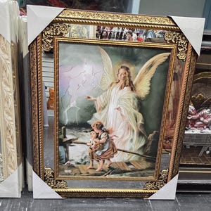 May include: A rectangular framed wall art piece featuring a guardian angel with large wings standing behind two children on a wooden bridge. The scene includes a stormy sky with lightning and a dark river. The frame is ornate, gold, and metallic.