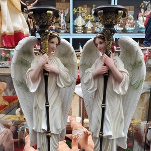 May include: Two white angel figurines with gold accents, each holding a black and gold candle holder. The angels are standing on black bases and have large white wings.