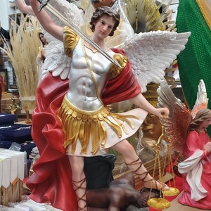 May include: A red and gold statue of the Archangel Michael, with wings, holding a sword and scales. He is standing on a demon, with the text "San Miguel" on the base.