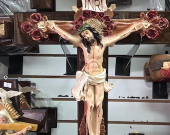 Può includere: Un crocifisso in legno con una figura scolpita di Gesù Cristo, ornata da una corona di spine e un perizoma. La croce è decorata con rose rosse e l'iscrizione "INRI".
